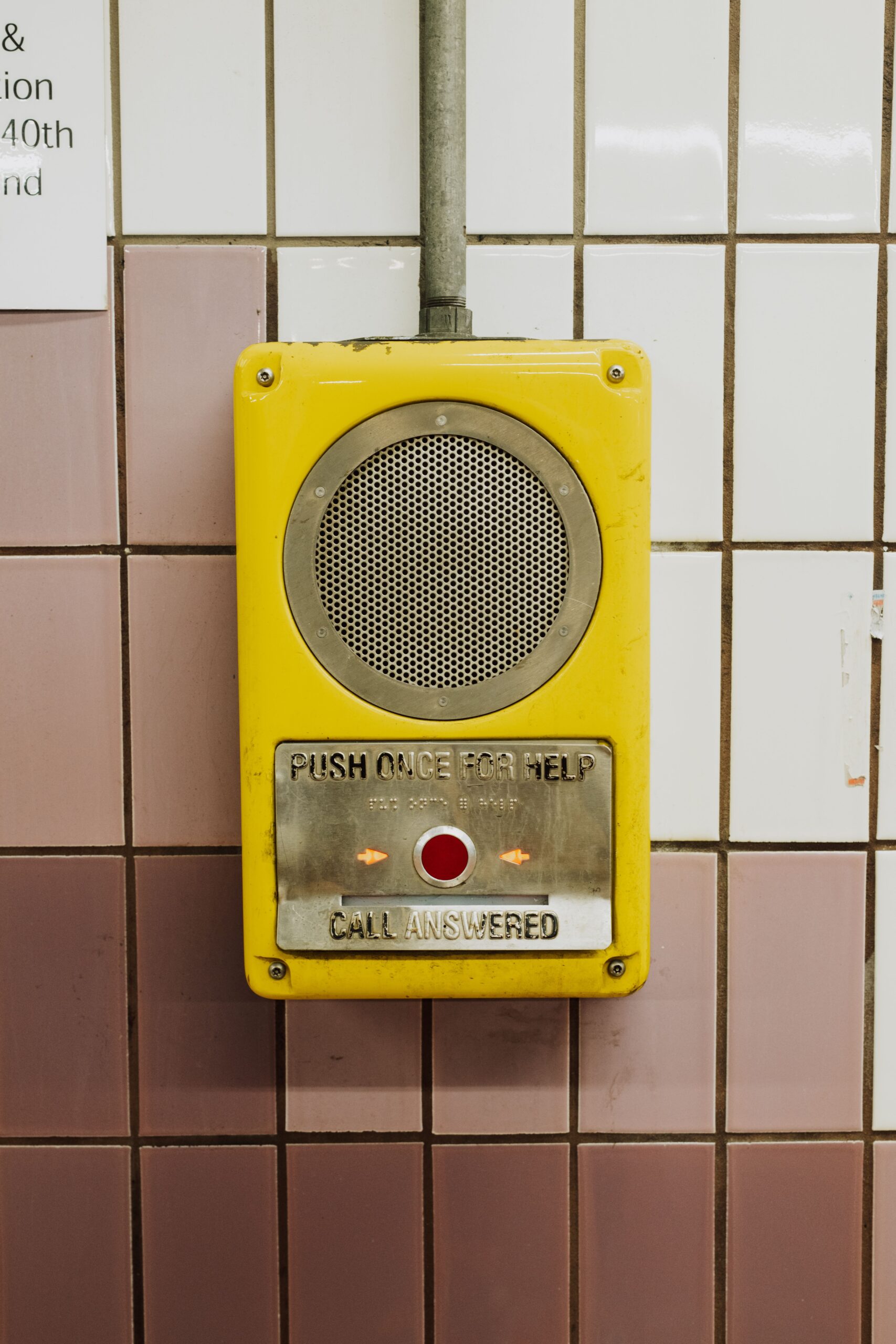 Yellow emergency call button with speaker grill mounted on tiled wall, reads'Push once for help' and 'Call answered' nearby