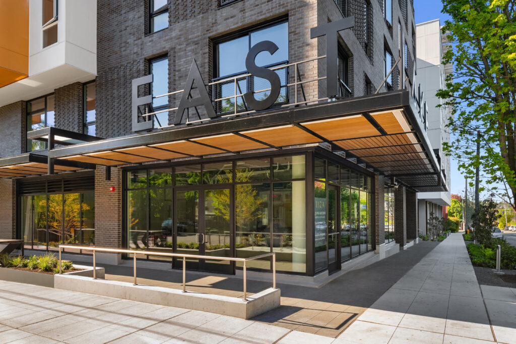 Modern brick office building with a large black 'EAST' sign above a glass storefront and wood-and-metal awning.