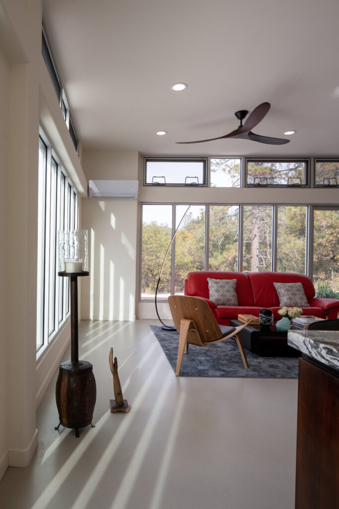 Bright living room with large windows, a red sofa, and modern seating under a ceiling fan and recessed lights.