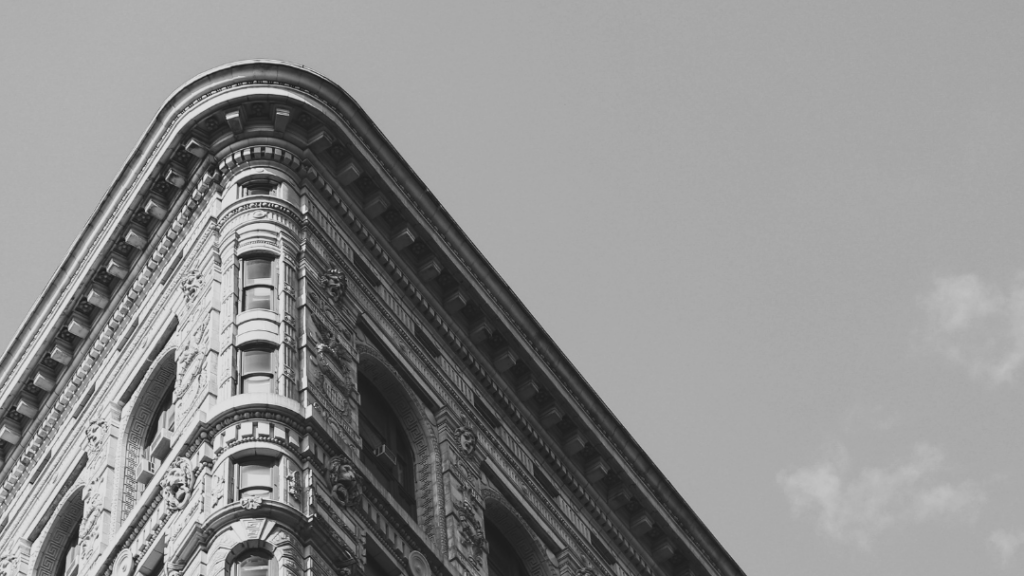 Corner of a historic, ornate brick building with arched windows and decorative details, seen from street level against a clear sky.